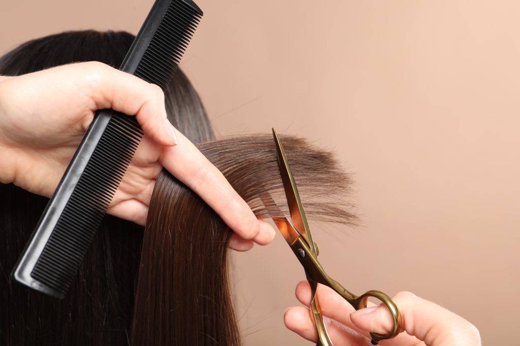 Hairdresser,Cutting,Client's,Hair,With,Scissors,On,Beige,Background,,Closeup.
